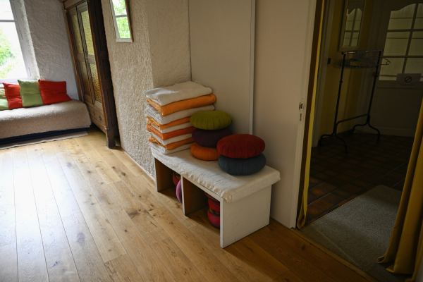 Coussins de méditation empilés sur un banc blanc, à l'entrée de la salle d'activités