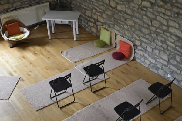 Tapis, coussins de méditation et chaises pliantes disposés sur le parquet de la salle d'activités